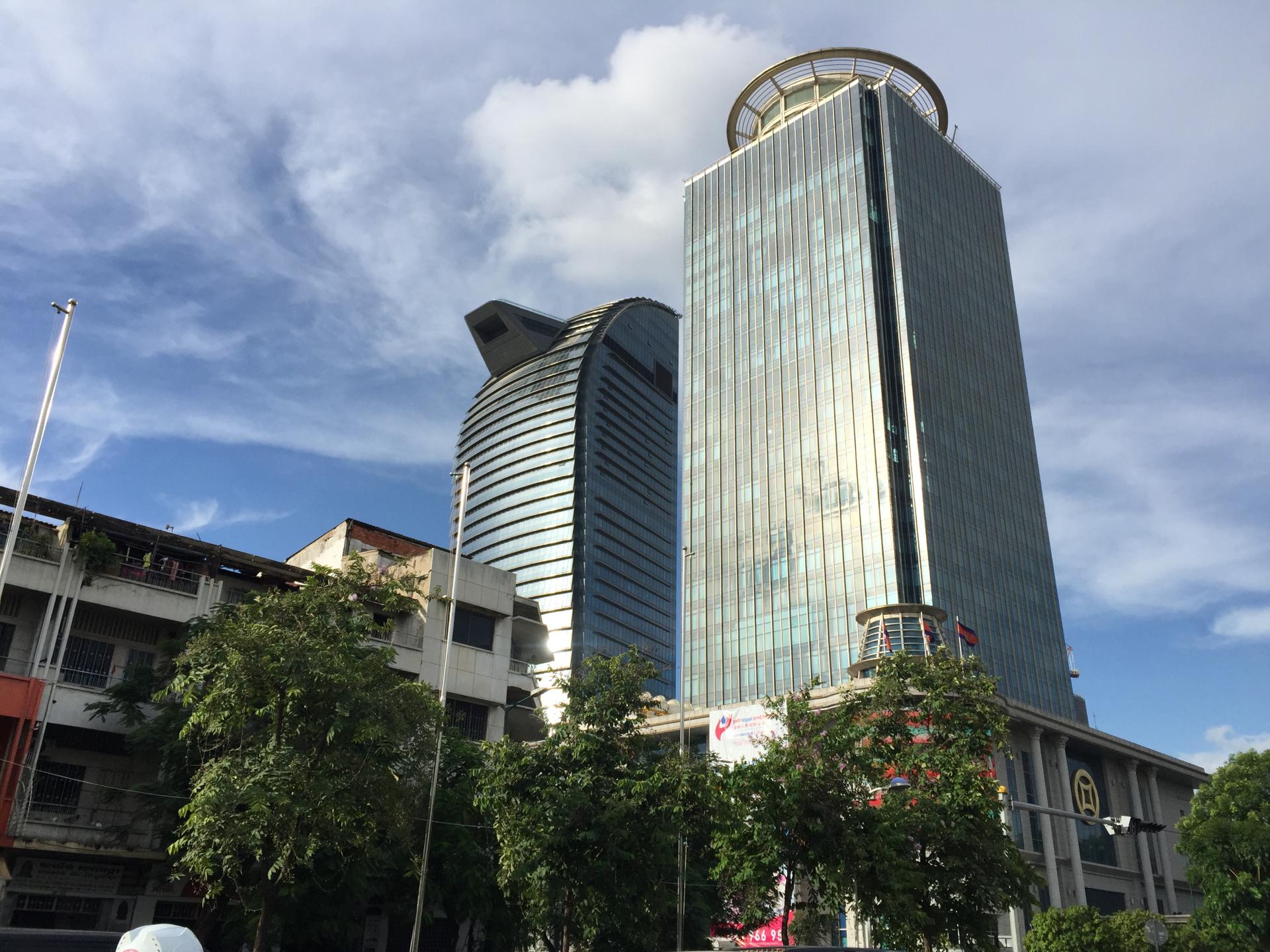 A view of modern office buildings in Phnom Penh, Cambodia, showcasing glass facades and surrounding trees under a blue sky.